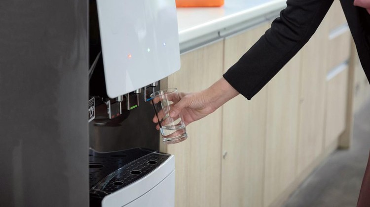 Woman hand holding glass filling cool water from water dispenser