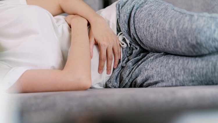 Asian woman having pain on her stomachache or Pelvic pain. housewife hands squeezing on the stomach while sitting on a sofa in the living room at home as suffering from menstruation cramp.