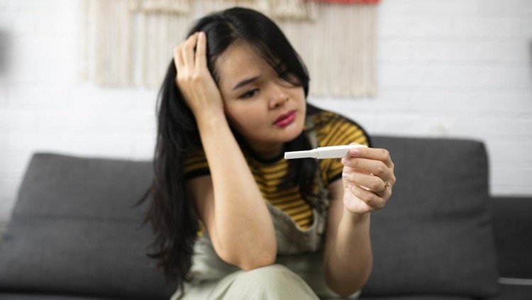 Asian young woman looking at pregnancy test with disappointed expression