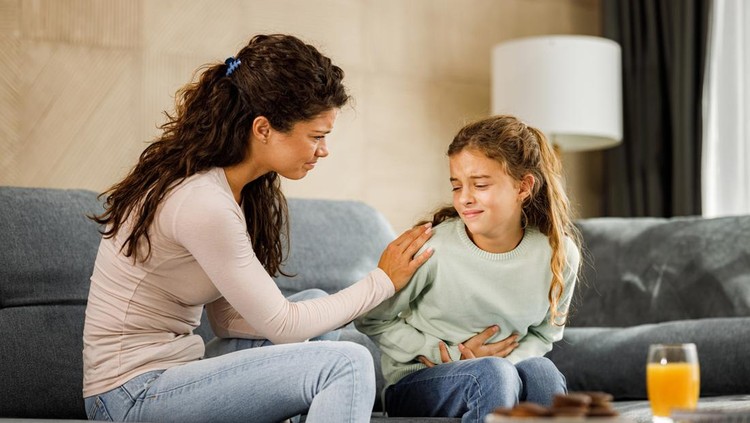 Worried single mother consoling her little girl who is having stomachache at home.
