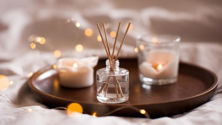 1343765164 Home perfume in glass bottle with wood sticks, scented burn candles tray in bedroom close up. Aromatherapy cozy atmosphere lifestyle. Winter warm xmas season.