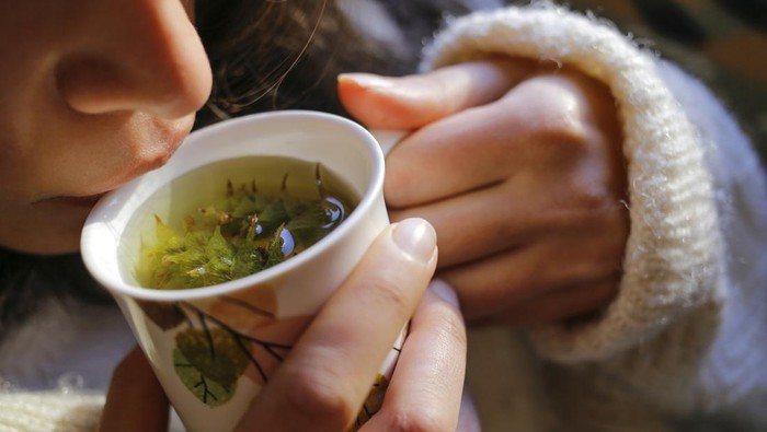 A young woman on the couch and with sage tea on the hand.