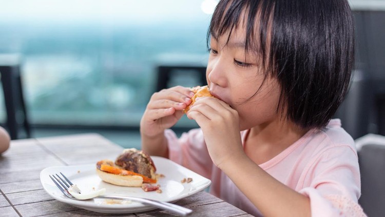 Ilustrasi Junk Food Picu Pubertas Dini Asian Little Chinese Girl eating hamburger in the outdoor cafe