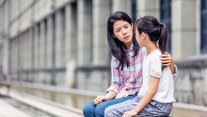 Caring mother calming and hugging crying upset little daughter, sitting at desk together, loving mum expressing support, comforting offended preschool girl, children psychologist concept