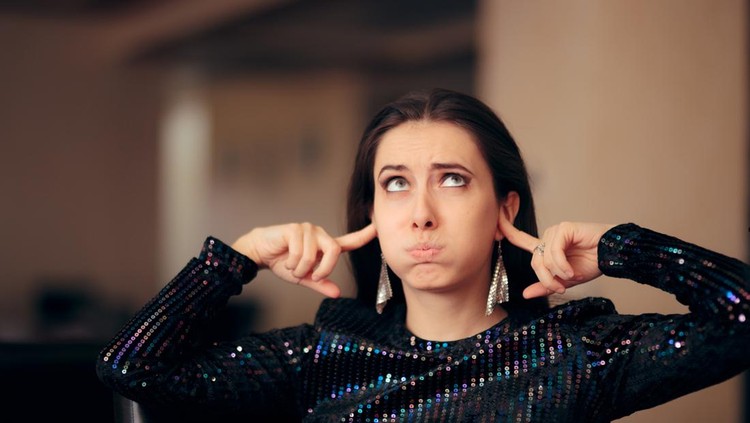 1070695836 Woman plugging her ears trying to cover loud noise