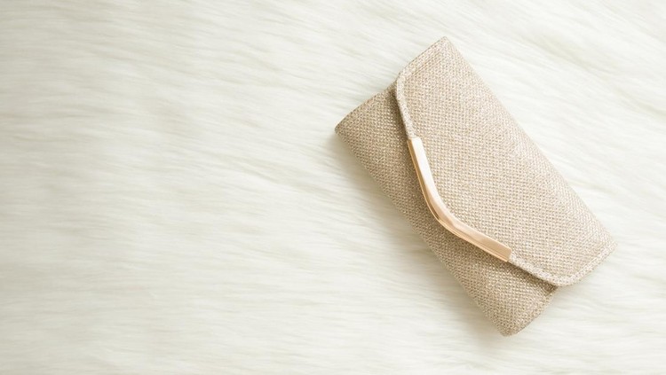 ilustrasi dompet paling mahal Shiny, golden clutch bag on white fluffy fur background. Woman accessory. Empty place for text. Closeup. Top down view.