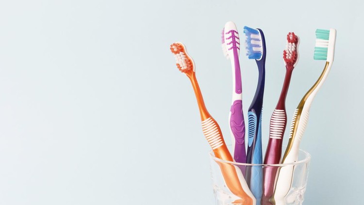 1130447045 Multi-colored toothbrushes in a glass cup, blue background