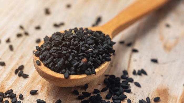 Black cumin seeds on wooden spoon on wooden background.