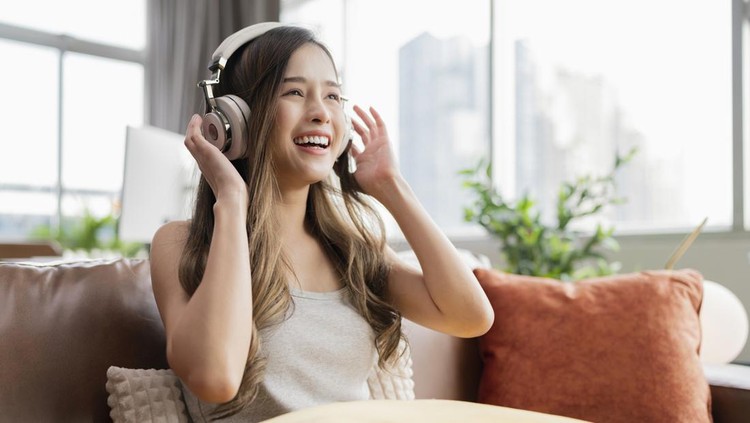 young attractive casual asian female woman watched the performance lives streaming concert in virtual reality through VR glasses headset goggle on sofa with fun and joyful moment in living room at home