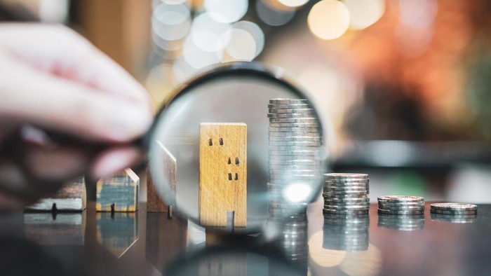 Hand holding magnifying glass and looking at house model, house selection, real estate concept.