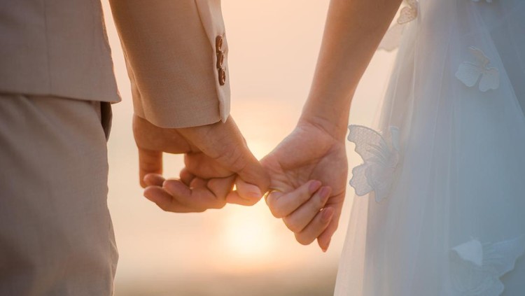 The bride and groom use the little finger together. lovely couple hold hand with sunset background