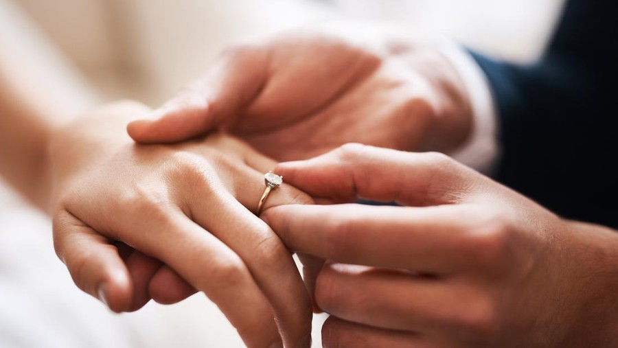 Ilustrasi Fakta Permintaan Pernikahan Dini Cropped shot of an unrecognizable groom putting a diamond ring on his wife's finger during their wedding