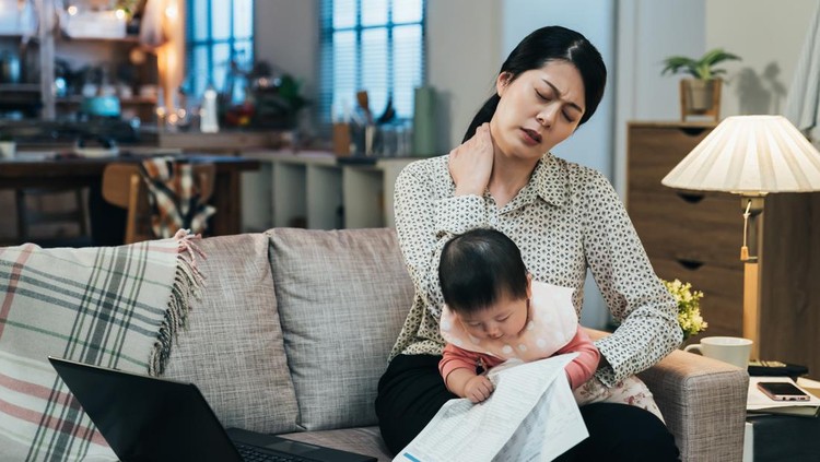 portrait asian working mother holding baby is having tension in her neck. millennial mom spraining her neck while looking after her child. lovely toddler is looking at document in her mother’s hand