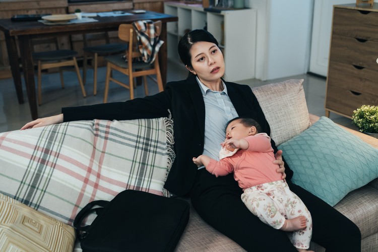 Ilustrasi Bunda Pekerja Alami Burnout portrait overwhelmed korean working mom sitting with her sleeping young kid on couch. asian career woman feeling worn out after putting child to sleep. pseudo-single parenting and lifestyle concept