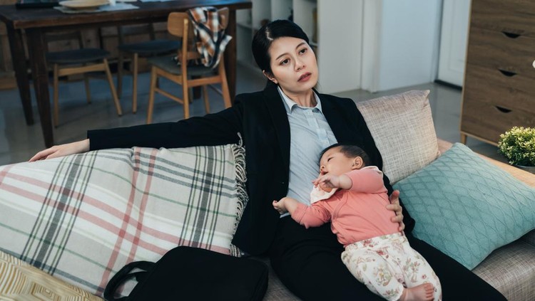 portrait overwhelmed korean working mom sitting with her sleeping young kid on couch. asian career woman feeling worn out after putting child to sleep. pseudo-single parenting and lifestyle concept