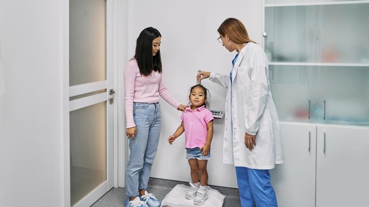 Pediatrician measures Asian female child's height during visit of child with her mother to medical clinic for consultation. Pediatrics