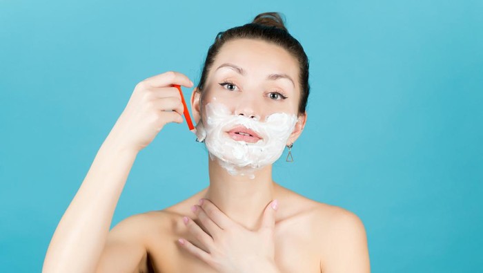 girl shaving her face with a disposable razor using shaving foam. Close up