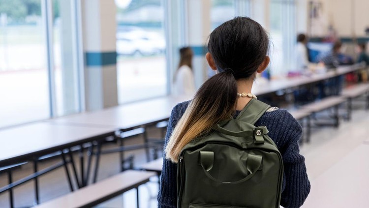 On the first day of school, the unrecognizable middle school girl carrying her backpack walks timidly into the cafeteria.