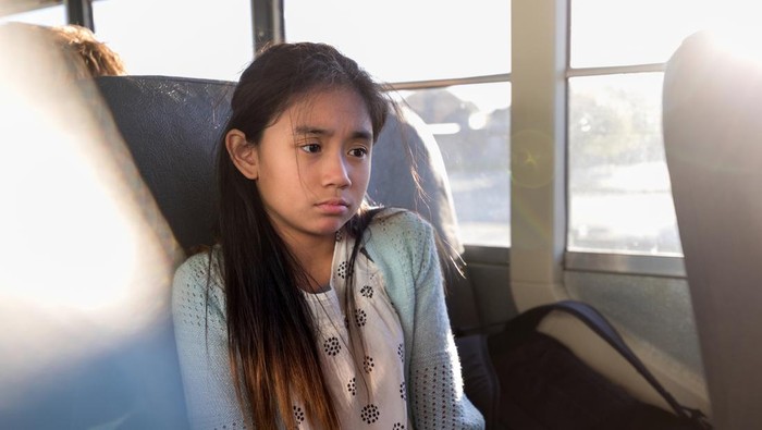 On the bus home from school, the young elementary school girl is sad after a hard day.