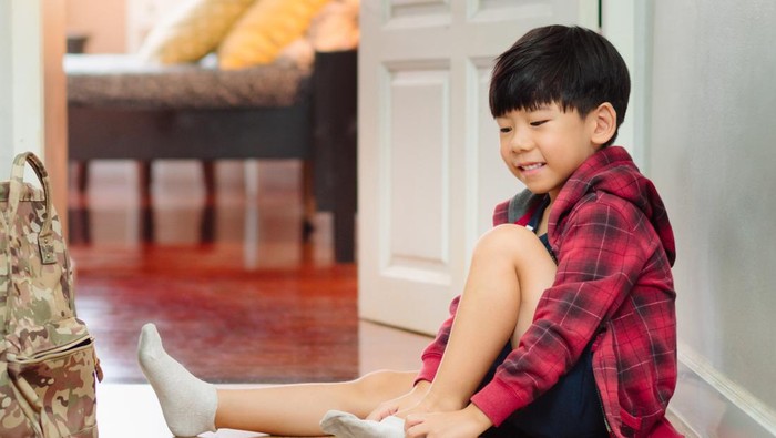 Small cute elementary age Asian boy learning and practicing putting on socks. Child sensory motor, muscle and sensory perception development stage in Montessori education. Self confidence and independence growth.