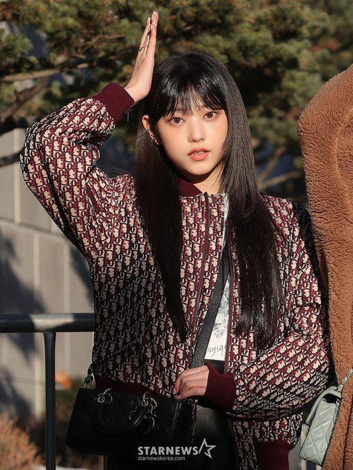 Gaya modis Haerin dalam perjalanan ke Music Bank pun mengenakan OOTD dari Dior. Sebuah outer maroon dengan logo Dior beserta tas ikonik Dior yang menawan melengkapi penampilannya./ Foto: Starnews