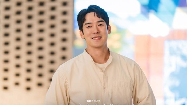 Yoo Yeon Seok berdiri di tengah panggung dengan pakaian kasual dan senyum ramah