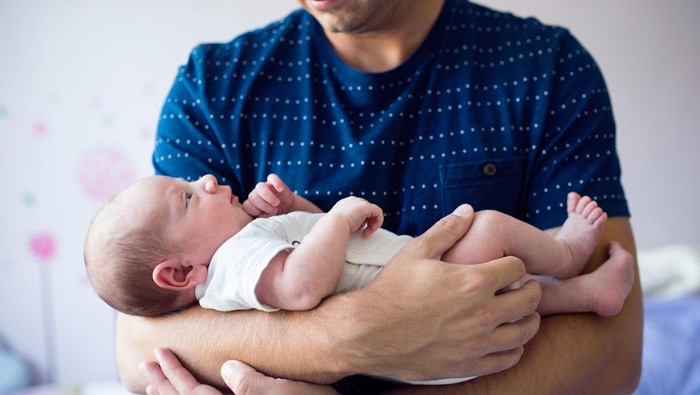 A proud father holding his newborn son wrapped in a blanket in the hospital