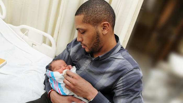A proud father holding his newborn son wrapped in a blanket in the hospital