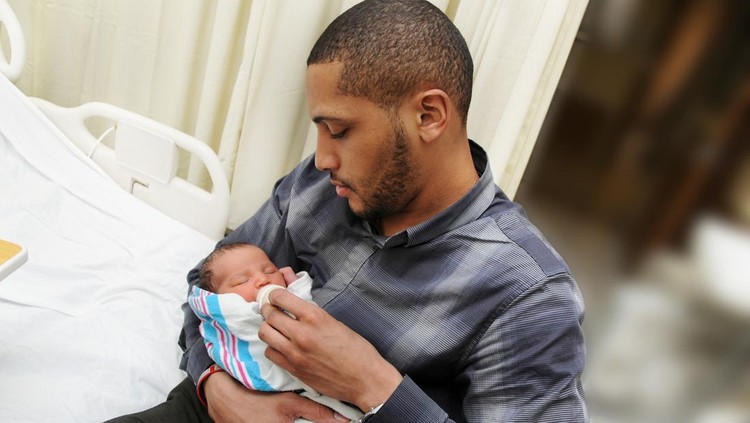 A proud father holding his newborn son wrapped in a blanket in the hospital