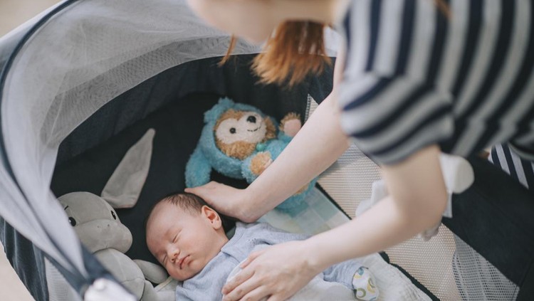 asian chinese young mother putting her infant baby boy in crib in bedroom