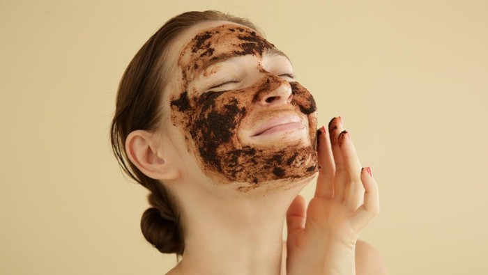 Woman exfoliating face with a coffee scrub, studio shot.