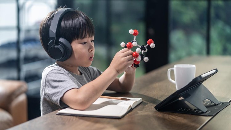 Asian little boy assembling molecular model by learning from home with school teacher teaching online. Homeschool kid practicing to think about logic and conference with teacher by remote application.