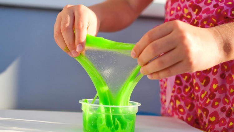 Ilustrasi Permainan Montessori Sesuai Usia Hand holding homemade toy called Slime, kids having fun and being creative by science experiment. Close up of a little girl is hand playing a green slime