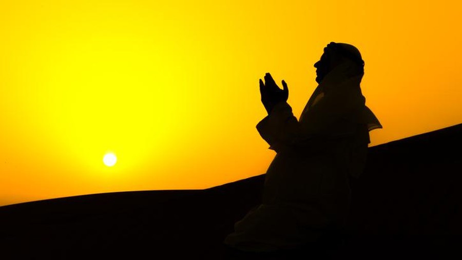An Arab man is praying over sand dunes of Dubai, United Arab Emirates