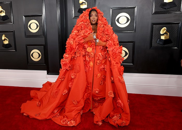 Nuansa whimsical ditampilkan Lizzo dalam mantel berhiaskan bunga karya Dolce & Gabbana. Di balik cape tersebut ia mengenakan gaun korset oranye. Foto: Getty Images/Amy Sussman