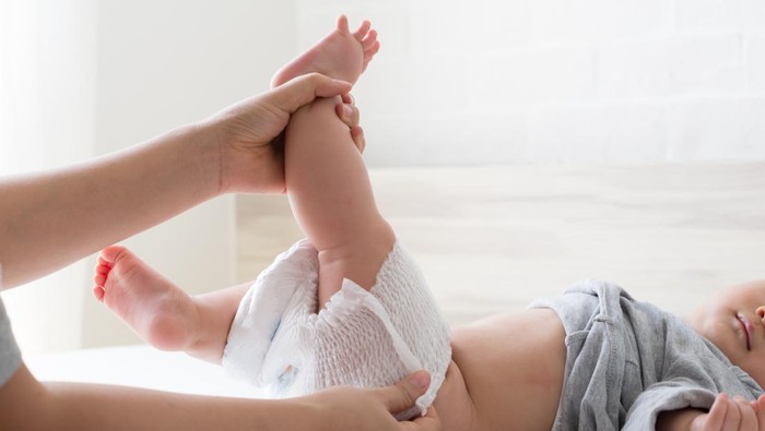 Mother changing diaper for her son on white bed in bedroom