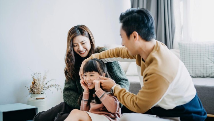 Young family having fun at home while father pinching daughter's cheek and laughing joyfully