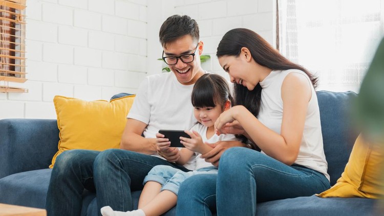 Happy Asian family using tablet, laptop, phone for playing game watching movies, relaxing at home for technology lifestyle concept