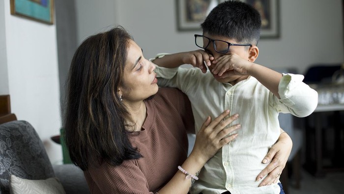 Caring mother comforting her little crying son at home