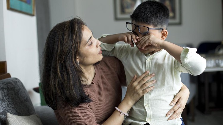 Caring mother comforting her little crying son at home