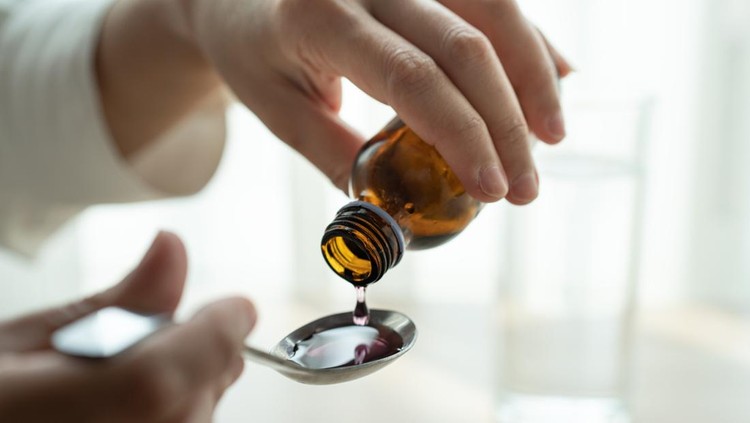 Woman hand pouring medication or cough syrup from bottle to spoo in Bangkok, Bangkok, Thailand