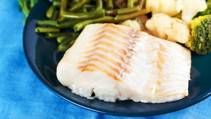 Fillet of boiled sea fish cod with broccoli, green beans and cauliflower on a blue plate, side view, close. Healthy diet dish for proper nutrition