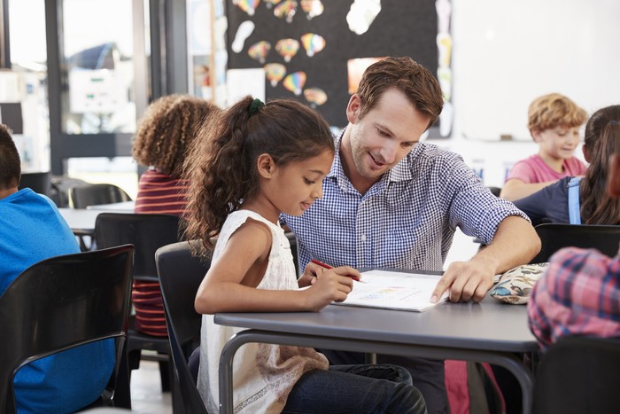 Teacher working with young schoolgirl at her desk in class