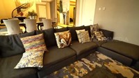 <p>Menyusuri area ruang keluarga yang tak ada sekat dengan meja makannya. Untuk ruang keluarga, Vio menambahkan sofa dengan warna gelap dan dilenkapi beberapa bantal dengan motif yang cukup unik. (Foto: YouTube TRANS7 OFFICIAL)</p>