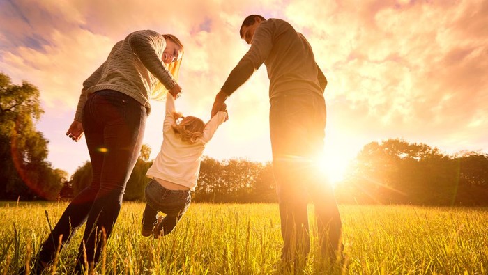 Happy family in the park evening light. The lights of a sun. Mom, dad and baby happy walk at sunset. The concept of a happy family.Parents hold the baby's hands.