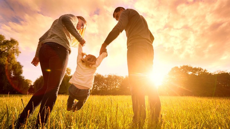 Happy family in the park evening light. The lights of a sun. Mom, dad and baby happy walk at sunset. The concept of a happy family.Parents hold the baby's hands.