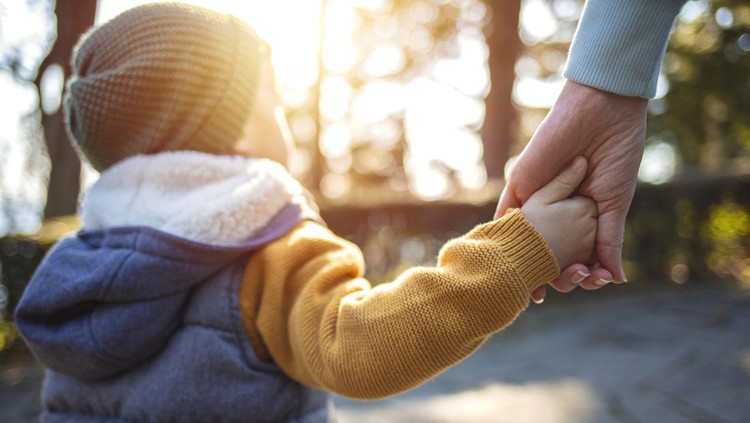 Happy family in the park evening light. The lights of a sun. Mom, dad and baby happy walk at sunset. The concept of a happy family.Parents hold the baby's hands.