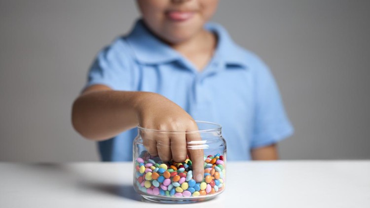 Little boy licking his lips while taking candy from the candy jar.