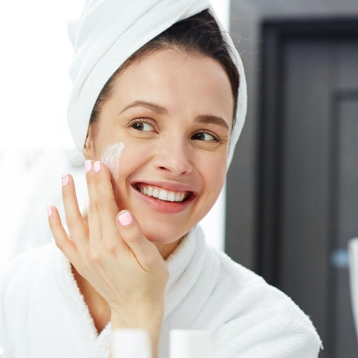 Potret seorang perempuan tengah memakai produk skincare.
