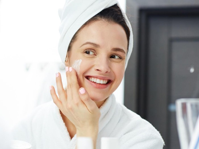 Potret seorang perempuan tengah memakai produk skincare.
